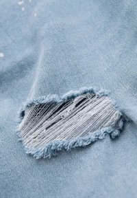 Ljusblå denimtyg med en fransad lapp med tydlig textur. Tåren avslöjar horisontella och vertikala trådar under.