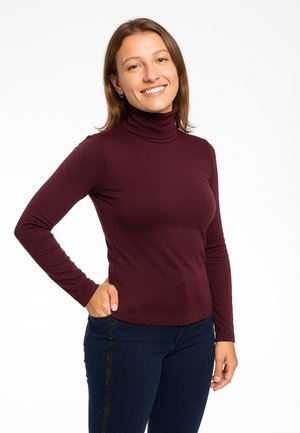 Maglia aderente bordeaux a collo alto realizzata in materiale elasticizzato con maniche lunghe, design attillato e texture morbida, abbinata a jeans scuri.