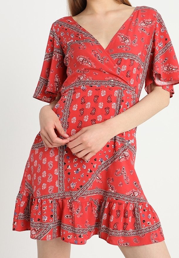 Rotes Wickelkleid mit V-Ausschnitt, kurzen Schmetterlingsärmeln und Rüschensaum. Besitzt Paisley- und Blumenmuster mit kontrastierenden Bordüren.