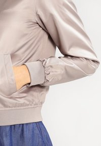 Satin bomberjack in lichtbeige met ribgebreide manchetten en tailleband; elastische mouwen; zijzakken geïntegreerd in de naad.