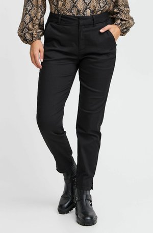 Schwarze, taillierte Hose aus glattem Stoff, mit Seitentaschen und slim fit. Kombiniert mit schwarzen Stiefeletten.