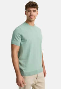 Mintgrøn kortærmet sweater med rund hals, ribbede manchetter og kant, fremstillet af blødt tekstureret materiale. Neutrale farvede bukser.