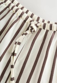 Gestreepte stof met een elastische tailleband en een gestrikte trekkoord. Kleuren zijn onder andere crème en bruin, met verticale strepen en een zachte textuur.