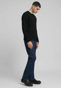 T-shirt noir à col rond et manches longues, jean en denim bleu et chaussures noires à enfiler. Le jean présente une légère décoloration et une coupe droite.