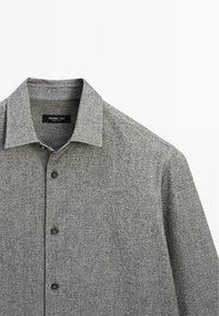 Camicia grigia con colletto classico, realizzata in tessuto misto. Presenta maniche lunghe e cinque bottoni neri sul davanti. Texture morbida.