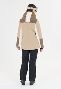 Giacca da sci in beige e marrone con una striscia bianca; presenta un cappuccio, maniche lunghe e pantaloni neri con cerniere all'orlo.