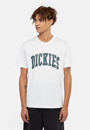 Valkoinen puuvillapaita, jossa on tumman teal-värinen kaareva teksti "DICKIES". Lyhyet hihat ja pyöreä kaula-aukko.