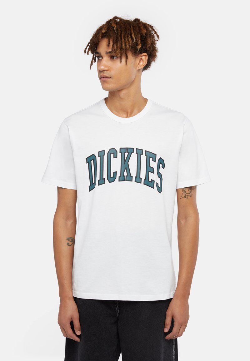Vit t-shirt i bomull med ordet "DICKIES" i mörk teal i en bågformad text. Korta ärmar och rund halsdesign.
