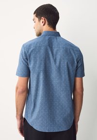 Koszula z krótkim rękawem w jasnoniebieskim kolorze z subtelnym wzorem, kołnierzykiem na guziki i zaokrąglonym dołem. Wykonana z teksturowanej tkaniny dla komfortu.