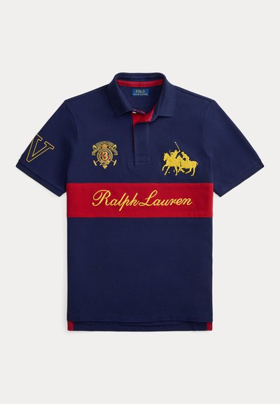 Teget plava polo majica s crvenom vodoravnom prugom, žutim vezom, uključujući konja i igrača, te natpisom "Ralph Lauren". Pamuk.