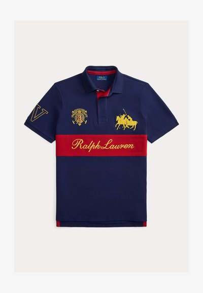 Teget plava polo majica s crvenom vodoravnom prugom, žutim vezom, uključujući konja i igrača, te natpisom "Ralph Lauren". Pamuk.