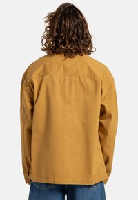 Oversized mosterdgele blouse met een rechte snit, gemaakt van katoen, met een rugpand en knoopdetails bij de mouwen.