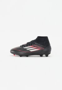 Black soccer cleat with a textured upper, red and silver accents, high ankle design, and conical studs for traction on grass surfaces.