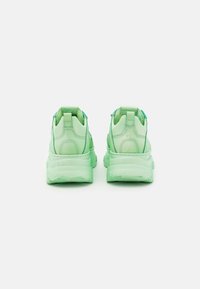 Valkkakengät vaaleanvihreänä, joissa on sileä synteettinen materiaali, pehmustettu nilkkaosa ja paksu läpikuultava pohja; varustettu kahdella vetoketjulla kantapäässä.