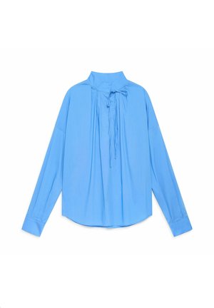 Blouse bleu clair à manches longues avec un col montant et un détail de nouage sur le devant, présentant une coupe décontractée et un tissu texturé.