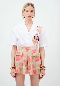 Camicetta bianca a maniche corte con ricamo floreale, abbinata a pantaloni corti rosa e verdi con motivo che presentano tasche laterali e una vestibilità comoda.