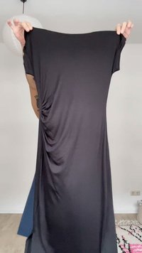 Άτομο που κρατά ένα μαύρο, κοντομάνικο φόρεμα τεντωμένο, δείχνοντας την υφή του υφάσματος και τις ρυτίδες σε φωτεινό φόντο.