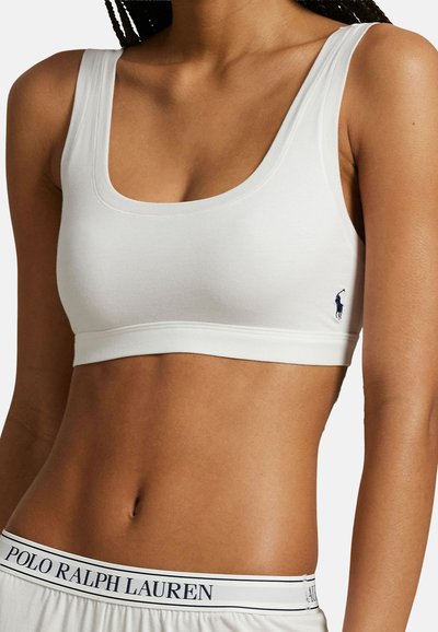 Γυναίκα που φοράει λευκό αθλητικό σουτιέν με μικρό λογότυπο Polo Ralph Lauren σε σκούρο μπλε στην πλευρά και σορτς με ελαστική μέση στο ίδιο χρώμα.
