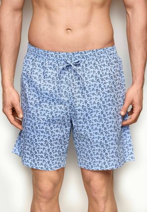 Uomo che indossa pantaloncini azzurri chiaro con un piccolo motivo floreale scuro e una vita elasticizzata con un nodo frontale a fiocco.