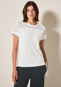 T-shirt blanc avec un design de bordure en maille sur les épaules, featuring des manches courtes et un ourlet à cordon. Fabriqué en tissu coton doux.