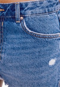 Pantalones cortos de mezclilla azul claro con un diseño desgastado, que presentan bordes deshilachados, costuras en contraste, un bolsillo delantero y un cierre de botón metálico.