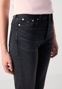 Sorte denimjeans med slim fit, med en liten frontlomme, sølvfarget metallhardware og subtil strukturert stoff. Detaljert søm er synlig.