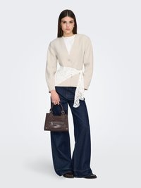 Beige Blazer mit V-Ausschnitt und Knopf, weißer Spitzen-Gürtel, weite dunkelblaue Jeans und eine kleine braune Handtasche mit Textur.