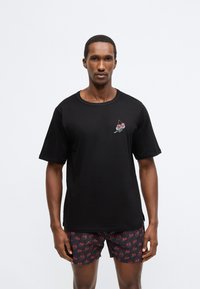 Tricou negru cu mâneci scurte, cu un desen cu cireșe pe pieptul stâng. Material moale, croială lejeră, asortat cu pantaloni scurți cu model.