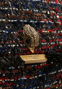 Kovový spon s tvarem ptáčí hlavy zdobený rhinestony na vícebarevném tkaném materiálu, s pozlacenou destičkou vyrytý "Kurt Geiger London."