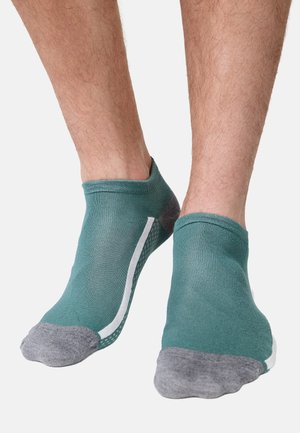 Knöchellange türkisfarbene Socken mit grauen Zehen und Fersen, getragen an nackten Füßen vor weißem Hintergrund.