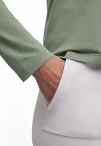 Langärmliges, hellgrünes Hemd aus weichem Stoff mit einem lockeren Schnitt, kombiniert mit weißen, strukturierten Hosen mit einer Seitentasche.