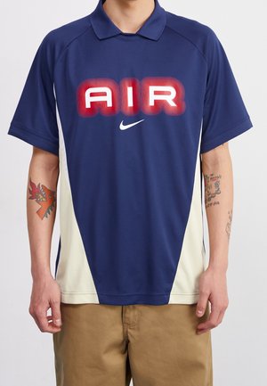 Polo bleu marine avec des panneaux latéraux crème, présentant un grand texte rouge "AIR" et un logo Nike blanc. Confectionné dans un tissu lisse et respirant.