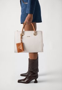 Borsa a tracolla bianca in pelle con dettagli in pelle marrone, hardware dorato e una piccola borsa attaccata. Ha una forma quadrata e manici corti.