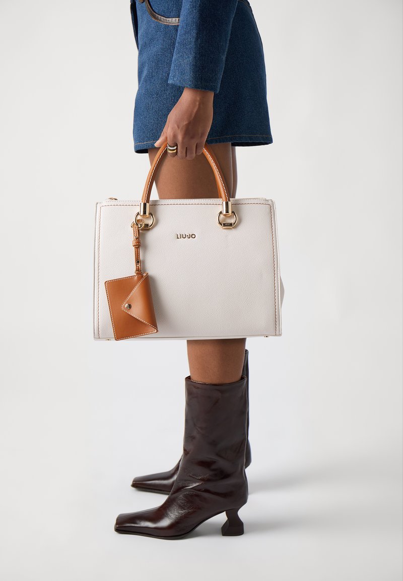 Borsa a tracolla bianca in pelle con dettagli in pelle marrone, hardware dorato e una piccola borsa attaccata. Ha una forma quadrata e manici corti.