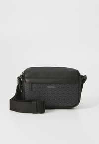 Geanta crossbody neagră Calvin Klein are un material texturat cu un model repetat de logo, accente din piele netedă și o curea ajustabilă.