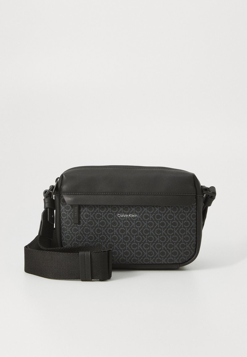 Geanta crossbody neagră Calvin Klein are un material texturat cu un model repetat de logo, accente din piele netedă și o curea ajustabilă.
