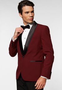 Chaqueta de esmoquin burdeos con solapa de pico de satén negro, un solo botón y dos bolsillos frontales. Lleva una camisa blanca y una pajarita negra.