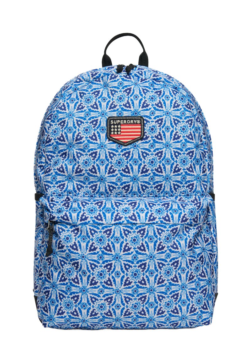 Mochila azul con un diseño de flores, hecha de tela. Presenta un bolsillo frontal con cremallera y un asa en la parte superior. Logo de la marca mostrado de manera prominente.