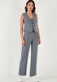 Gray sleeveless vest with front buttons, paired with matching wide-leg pants, made from textured fabric, styled with white sneakers.