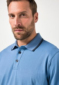 Vaaleansininen polo-paita, jossa on kaksinappinen nappilista, mustaviiruinen kaulus ja pehmeä koostumus. Ominaisuuksiin kuuluu klassinen istuvuus ja minimaalinen yksityiskohtaisuus.