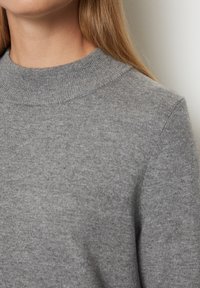 Maglione grigio a maglia con colletto alto a costine, texture morbida e dettagli di cucitura minimi, visto dalla spalla in su.