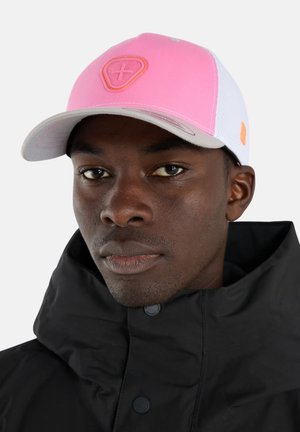 Homme portant une veste noire et une casquette rose et blanche avec un logo bouclier brodé et une croix sur le devant, expression neutre, fond clair.