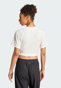 Bílé zkrácené tričko s krátkými rukávy, na zádech s malým logem Adidas. V kombinaci s černými skládacími sportovními kalhotami.