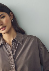 Long-sleeve, collared shirt in muted brown fabric with a smooth texture; features button placket and slightly oversized fit.
