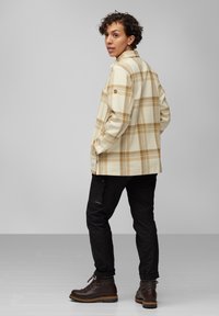 Rutet skjorte i krem og brun, med knap-d design og sidelommer, kombinert med svarte bukser og brune snøresko.