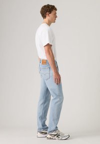 helehallid sirge lõikega teksapüksid, pruun nahast tagumine märk ja külgvaade, kus on valge T-särk ning mitmevärvilised tossud.