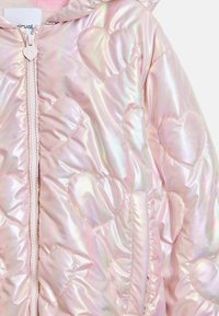 Iridescent rosa puffjacka med ett hjärt-mönster, med dragkedja och huva. Mjuk, slät textur med vadderade sektioner.