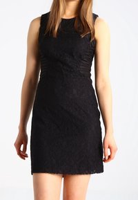 Svart spetsklänning med en figurnära siluett, ärmlös design, intrikat blommönster och en scalloped fåll.