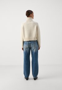 Lyse beige strikkegenser med høy krage og ribbestrikkede kanter, kombinert med lyseblå, falmede vide jeans. Minimalistisk design.