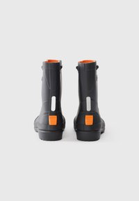 Bottes de cheville en caoutchouc noir avec surface texturée, accents orange au niveau du talon et détails réfléchissants. Semelle épaisse pour une meilleure traction.